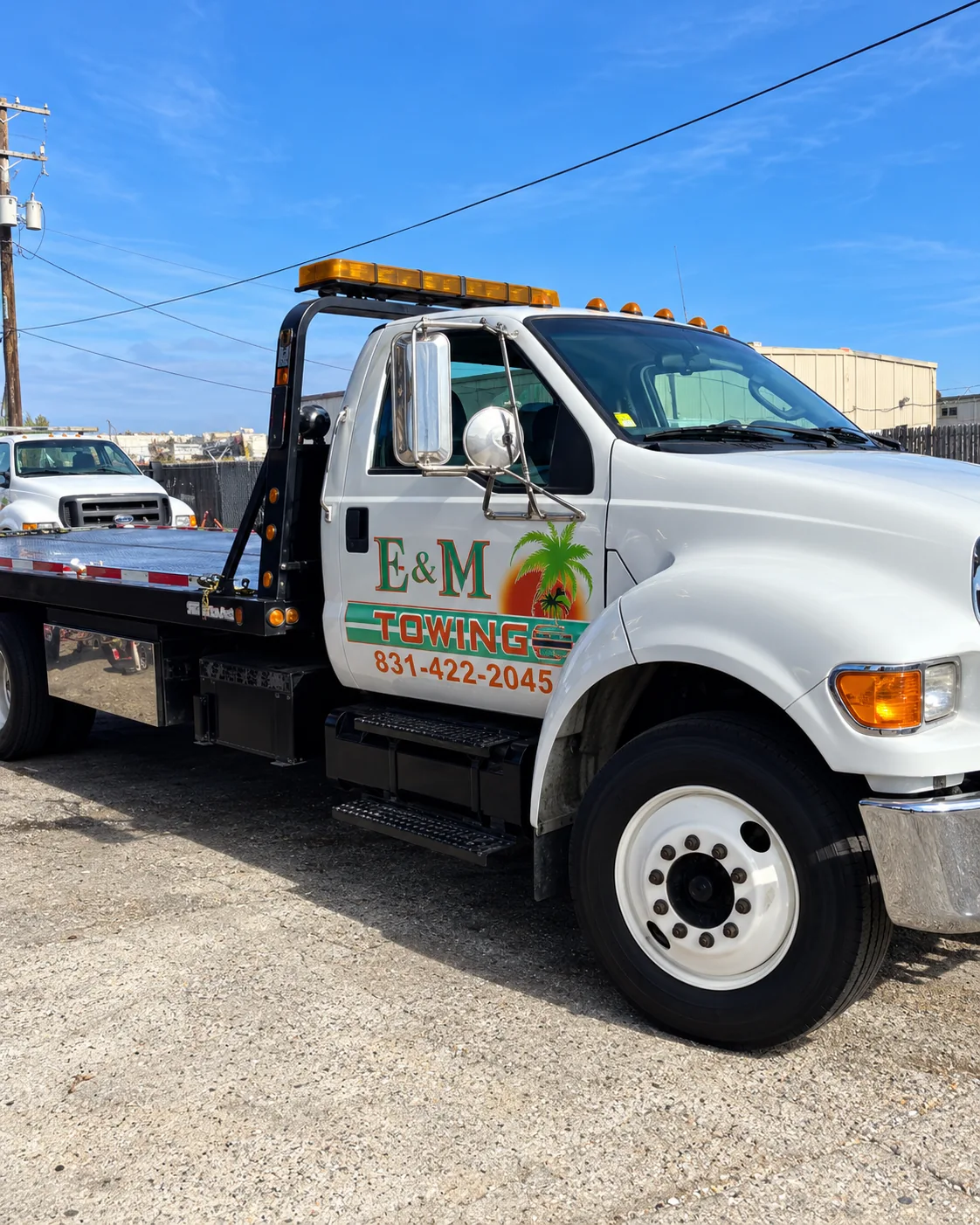 White E&M Towing flatbed truck parked in an industrial yard, with its branded cab clearly visible.